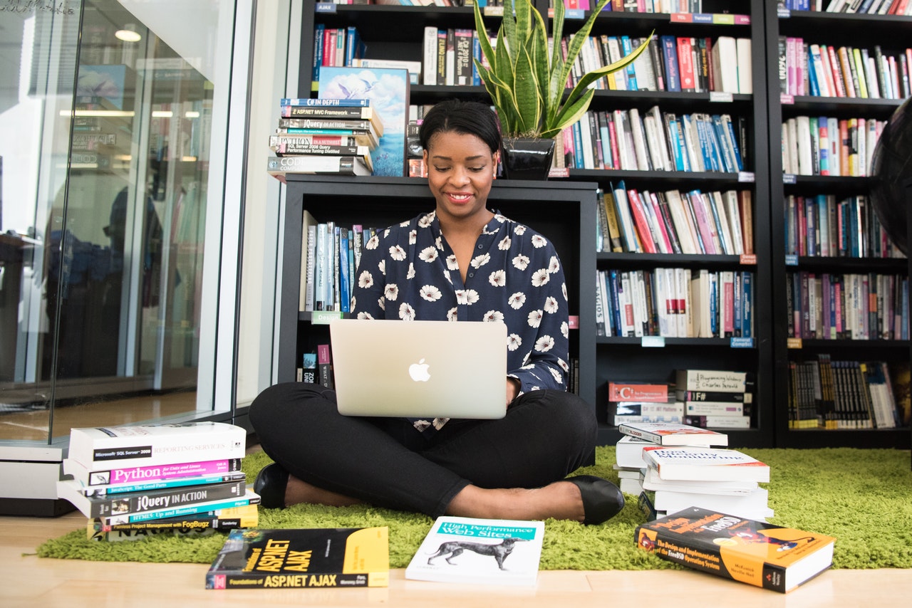 Student engrossed in reading on her laptop, surrounded by a stack of books